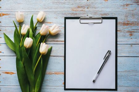 White bouquet of tulips on wooden blue background with blank paper tabletの写真素材