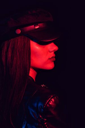 fashion portrait of a girl in profile in a leather cap and jacket with a red neon light