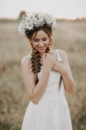 happy smiling girl with braids and floral wreath in white dress in boho style in summer outdoorsの写真素材