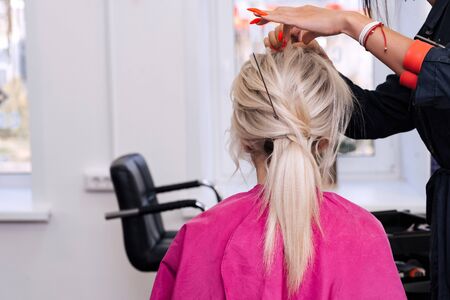 hands of a professional hairdresser make a low bun hairstyle for a blonde girl with long hair in a beauty salonの写真素材