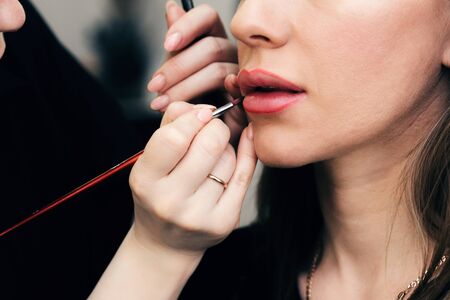 make-up artist paints lips with a lip brush for a woman in a beauty salon