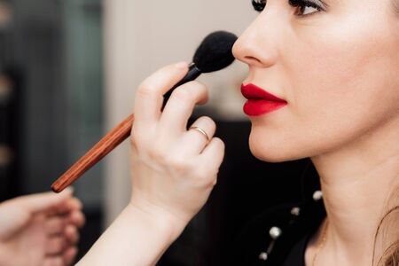 professional makeup artist puts powder brush in hand on the face of a womanの写真素材