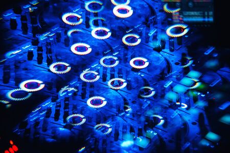 DJ mixer in a nightclub with a background of glowing lights from buttonsの写真素材