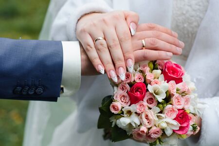 hands of the bride and groom with wedding gold rings on the background of a beautiful floral bouquetの写真素材
