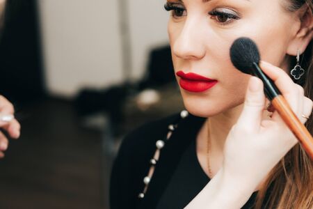 professional makeup artist puts powder brush in hand on the face of a womanの写真素材
