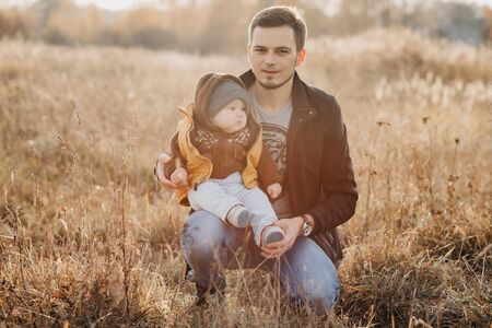 young dad with son boy child sitting in nature in autumn