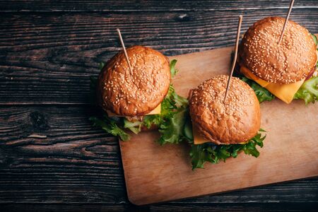 three hamburgers with meat, cheese, lettuce, tomato on a Board on a wooden table. The view from the top, flay layの写真素材