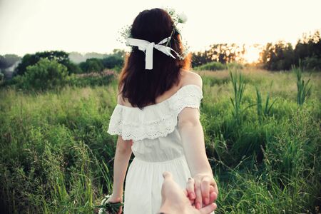 Follow me concept. Back of a girl holding her boyfriend's hand in a field in natureの写真素材