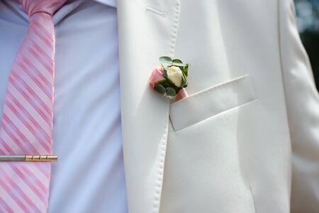 boutonniere of fresh rose flower on the groom's suit on the wedding day close-upの写真素材