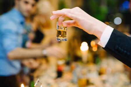 mans hand holding a glass of vodka in a restaurant on a holidayの写真素材