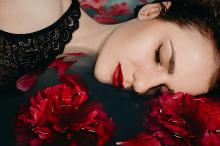 portrait of girl with makeup enjoying in bath with red flower petalsの写真素材