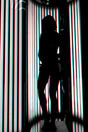 girl in the vertical Solarium. Silhouette on the background of ultraviolet lampsの写真素材