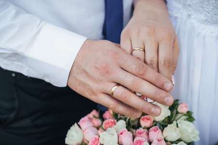 hands of the bride and groom with gold rings on the background of the wedding bouquetの写真素材