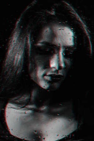 black and white portrait of a girl with closed eyes behind glass with raindropsの写真素材