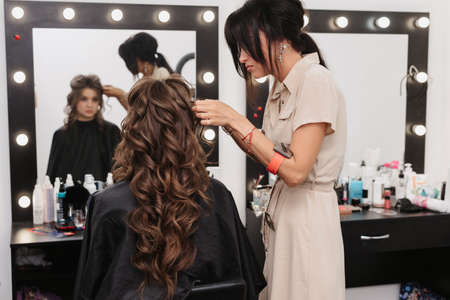 girl with brown curly long hair in a beauty salon. Morning preparation of the brideの写真素材