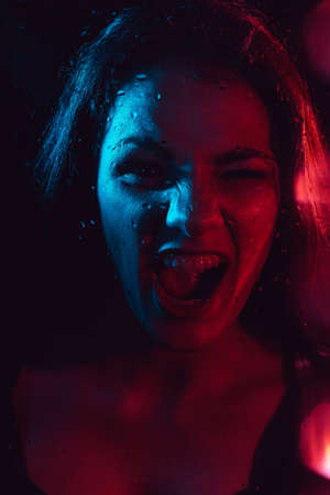 Sensual portrait of a screaming girl behind glass with raindrops