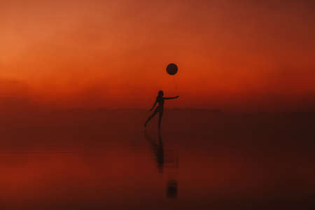 silhouette of a girl practicing a yoga exercise in a pose on the waterの写真素材