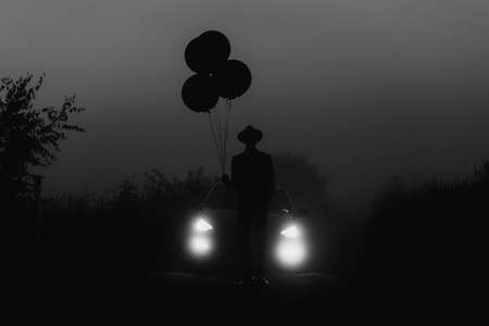 dark silhouette of a man in a hat with balloons in his handの写真素材
