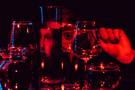 portrait of a strange man looking through a magnifying glass with a large eye and glasses of waterの写真素材