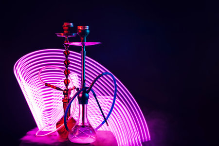 two hookahs with pipes and bowls and a flask of water with purple neon lighting