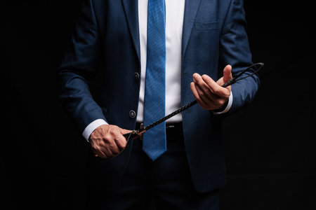 Male dominant businessman in a suit holding a leather whip Flogger for dominationの写真素材