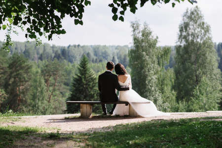 couple bride and groom embrace sitting on a bench on a wedding day in summerの写真素材