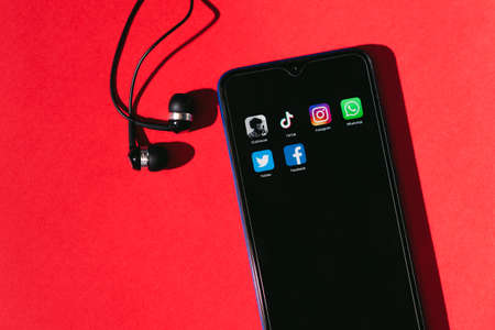 VICHUGA, RUSSIA - FEBRUARY 17, 2021: smartphone with icons of trending social apps on the screen lies on a red background with headphonesのeditorial素材