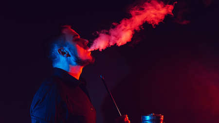 male smoker smokes a hookah in a shisha and lets out a cloud of smoke