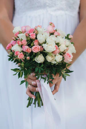 wedding bouquet with pink and white roses in the hands of the brideの写真素材