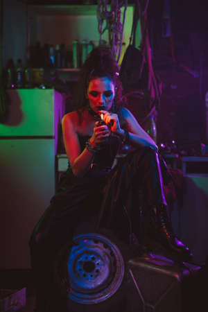 girl in a futuristic cyberpunk costume smokes a cigarette with a neon light in the garage. Steampunk styleの写真素材