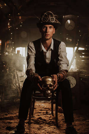male inventor in a steampunk suit in a top hat with glasses with a golden skull in his hand