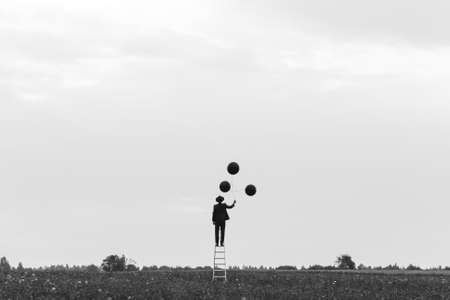surreal silhouette of a man in a suit standing on the stairs in a field with balloonsの写真素材