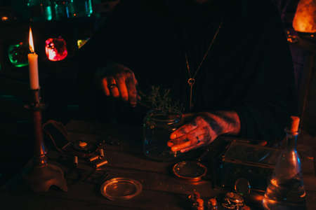 hands of sorcerer alchemist prepare a magic potion poison with herbs in flask at tableの写真素材