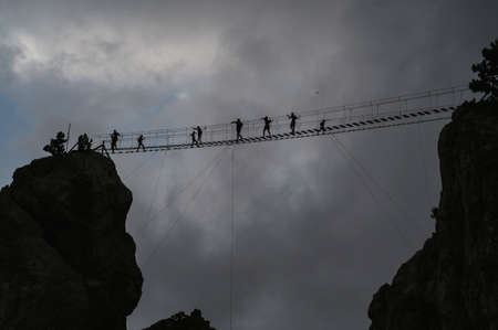 Silhouettes of people passing a dangerous suspension bridge on top of Ai-Petri Mountain in Crimeaの写真素材