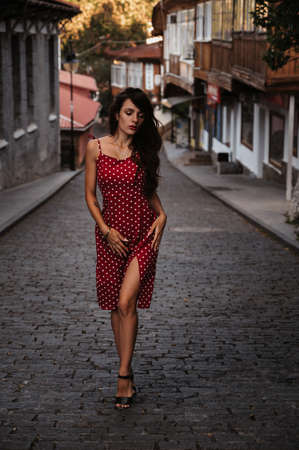 Sexy young Caucasian girl in red dress posing on beautiful historical street in Europeの写真素材