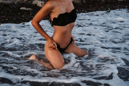 slender body of a sexy girl erotically sitting on her knees in the water in the waves of the seaの写真素材