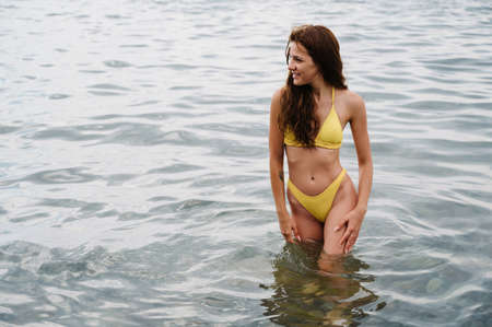 slender girl in a yellow swimsuit in the water in sea in summer