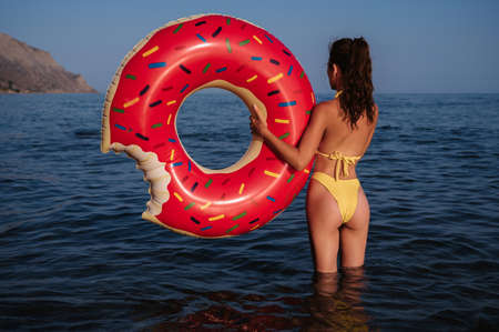 slender girl with a sexy booty in a swimsuit holds an inflatable circle in her hands on a sunny summer day at the seaの写真素材