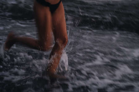 Legs of a girl in a swimsuit running along the shore on the beach by the sea