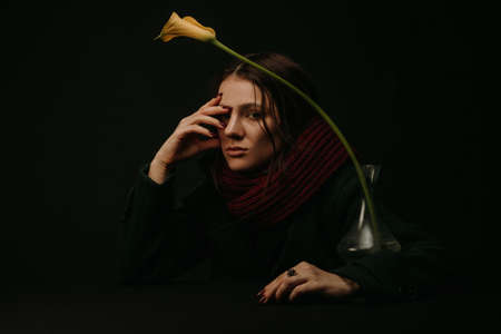 dramatic portrait of a girl in a coat and scarf with a flower in the vintage styleの写真素材