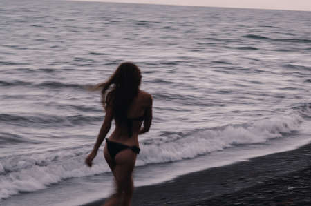 happy girl in a swimsuit happily runs and freedom on the beach by the sea with waves
