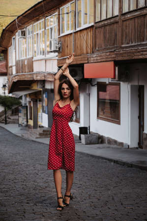 Sexy young Caucasian girl in red dress posing on beautiful historical street in Europeの写真素材