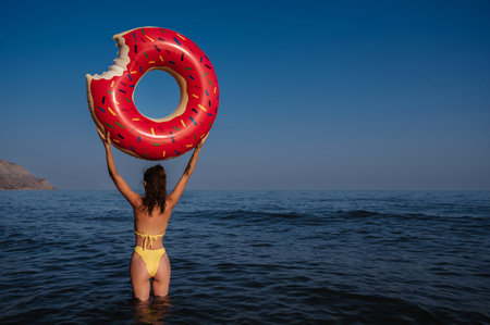 slender girl with a sexy booty in a swimsuit holds an inflatable circle in her hands on a sunny summer day at the seaの写真素材