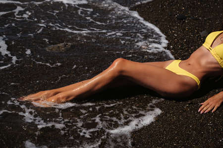 slender sexy body of a girl in a swimsuit lying on the beach by the seaの写真素材