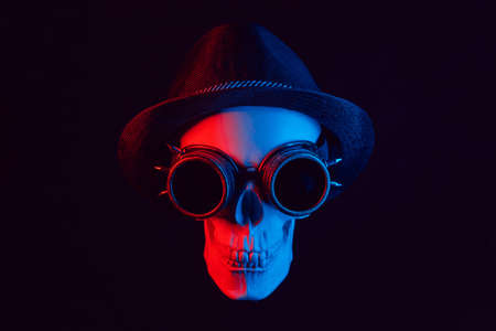 human skull in steampunk glasses and a hat with red and blue lightの写真素材