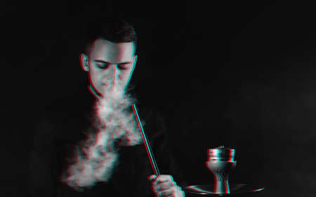male smoker smokes a hookah and lets out a cloud of smokeの写真素材