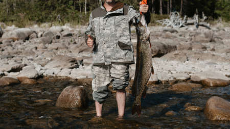 male fisherman holds a large pike caught on the shore of the lake