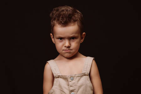 serious upset boy in overalls with a stylish hairstyle