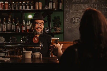 smiling bartender serves draft beer in a glass at the bar to a woman
