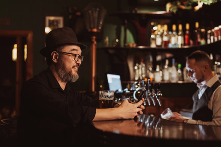 happy smiling man uses a mobile phone smartphone while sitting at bar counter with a beerの写真素材